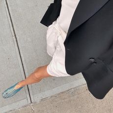 NYC based fashion influencer Courtney Grow walking outside wearing a black blazer, white shorts, and The Row blue Mara jelly flat sandals