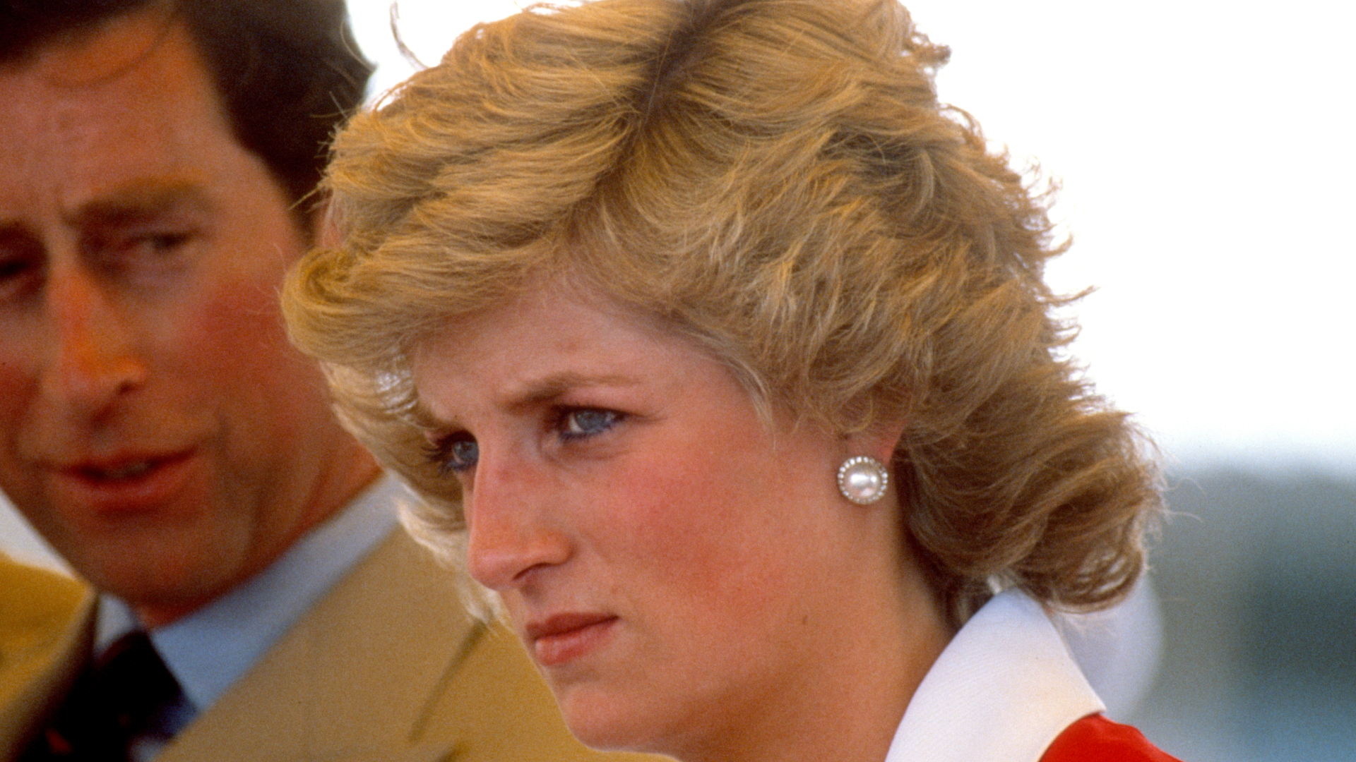 Princess Diana scowling wearing a red and white dress