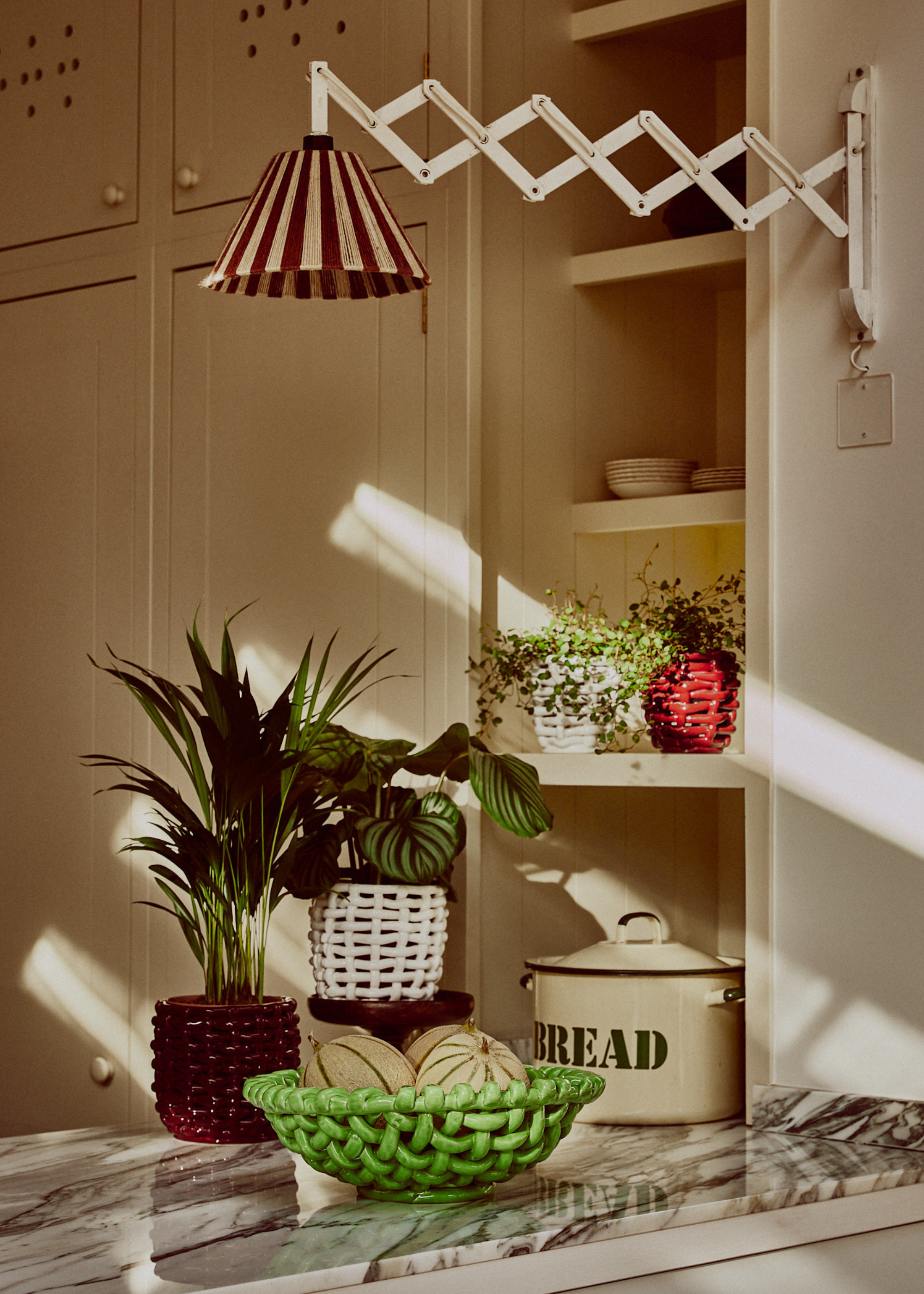 A kitchen counter with a woven bowl of fruit, a couple of woven planters and a bread box