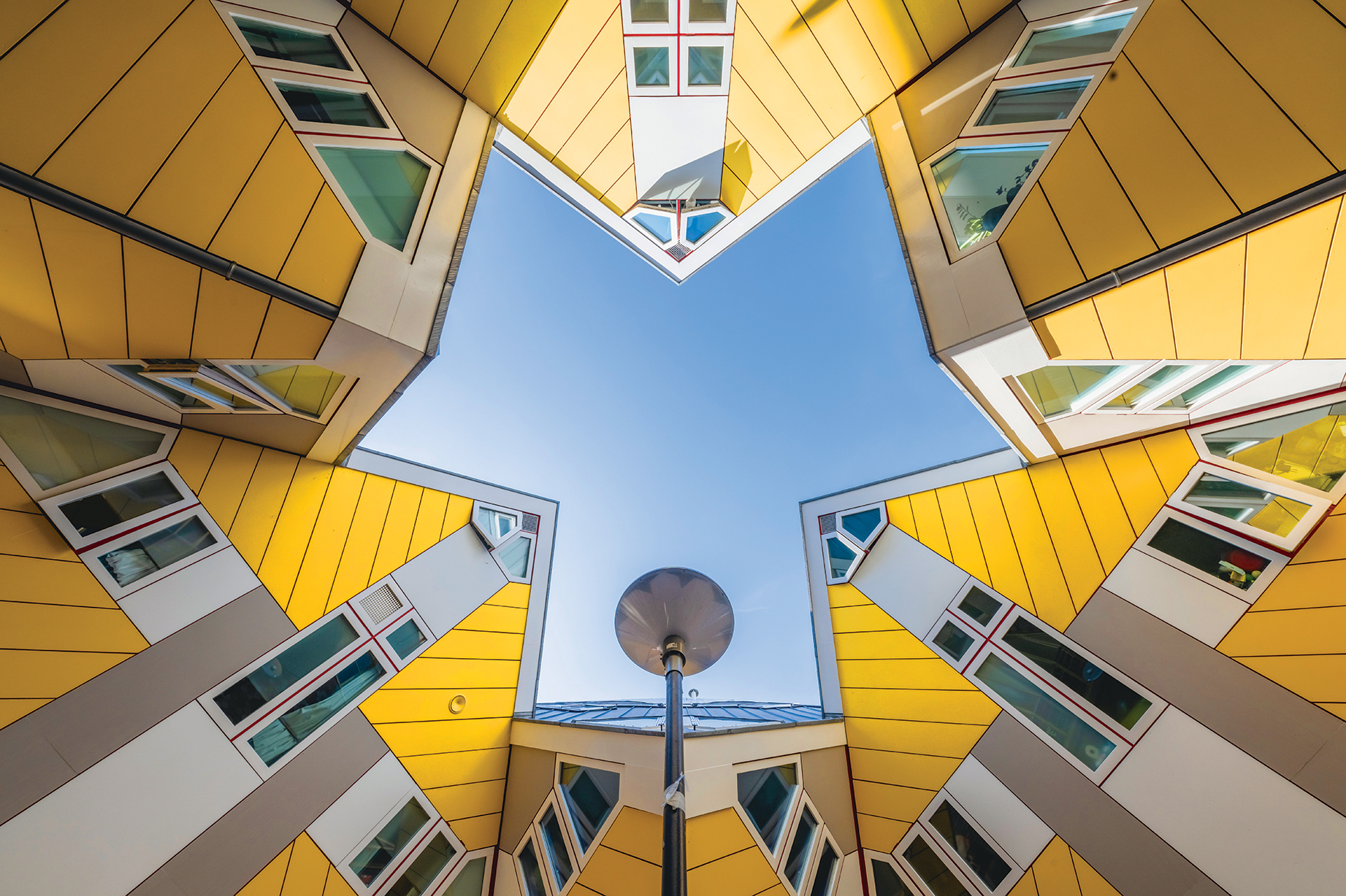 A star-shaped view looking up at modern buildings with yellow façades and colorful windows against a clear blue sky