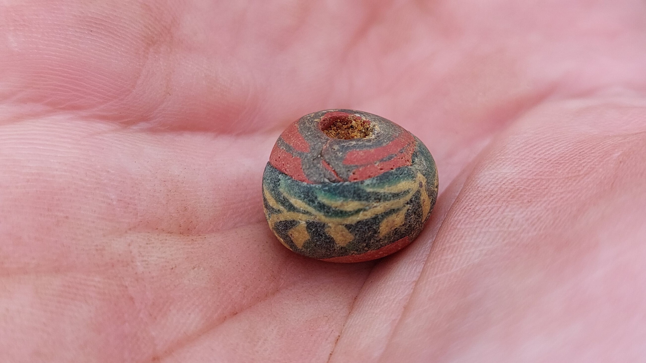 A large dark bead with yellow floral motif found in the Goth cemetery shown in palm of hand.