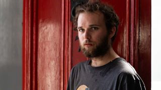 MAXIMILLIAN FAIRLEY as Martin 'Marty' Baines wearing a dark tshirt and standing in front of a red door