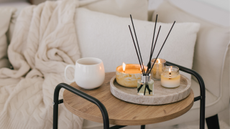 small table holding three candles, a reed diffuser, and a white coffee mug