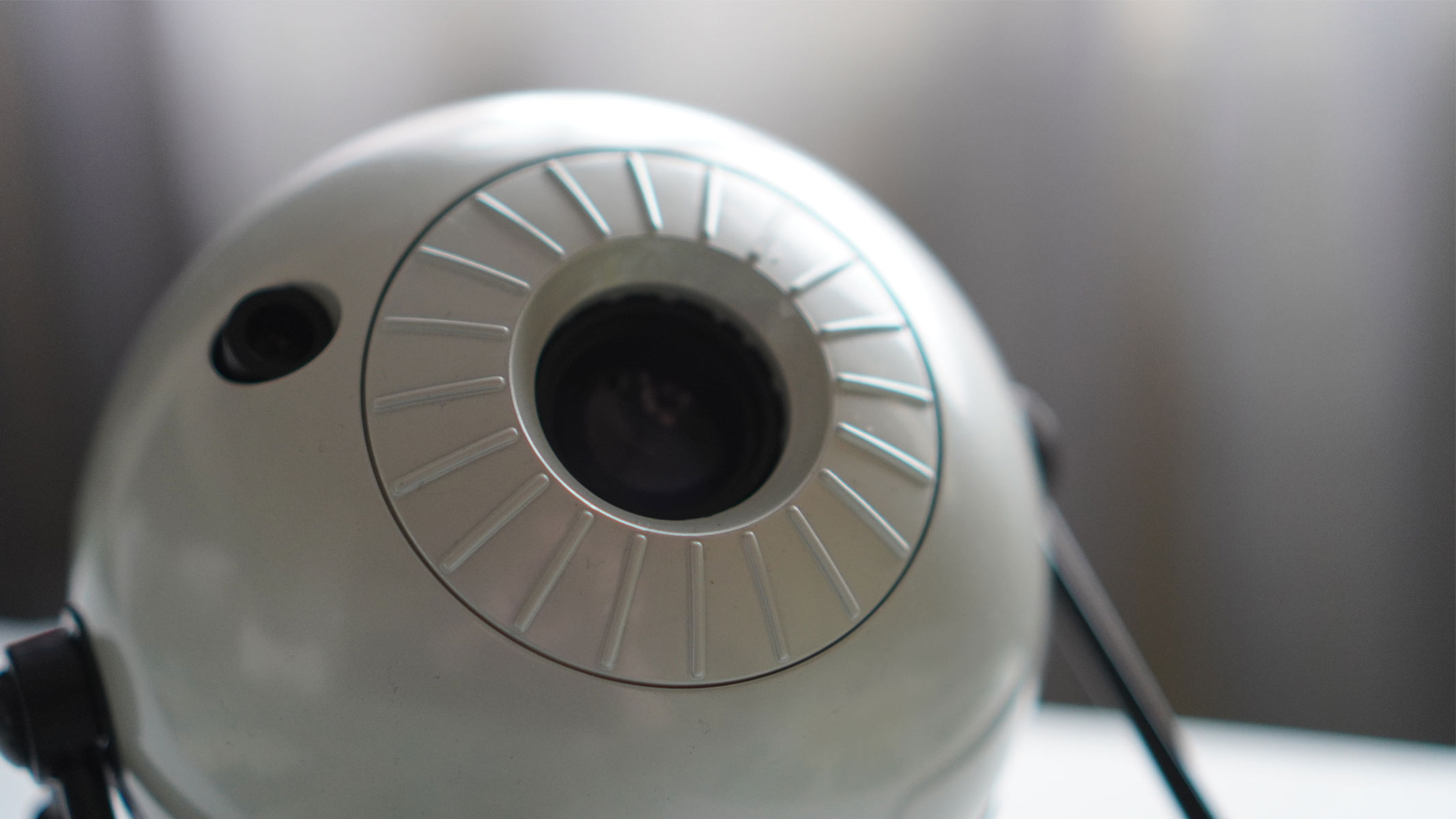 A white sphere is on a black legged stand on a white surface and we can see a close up of a black lens.