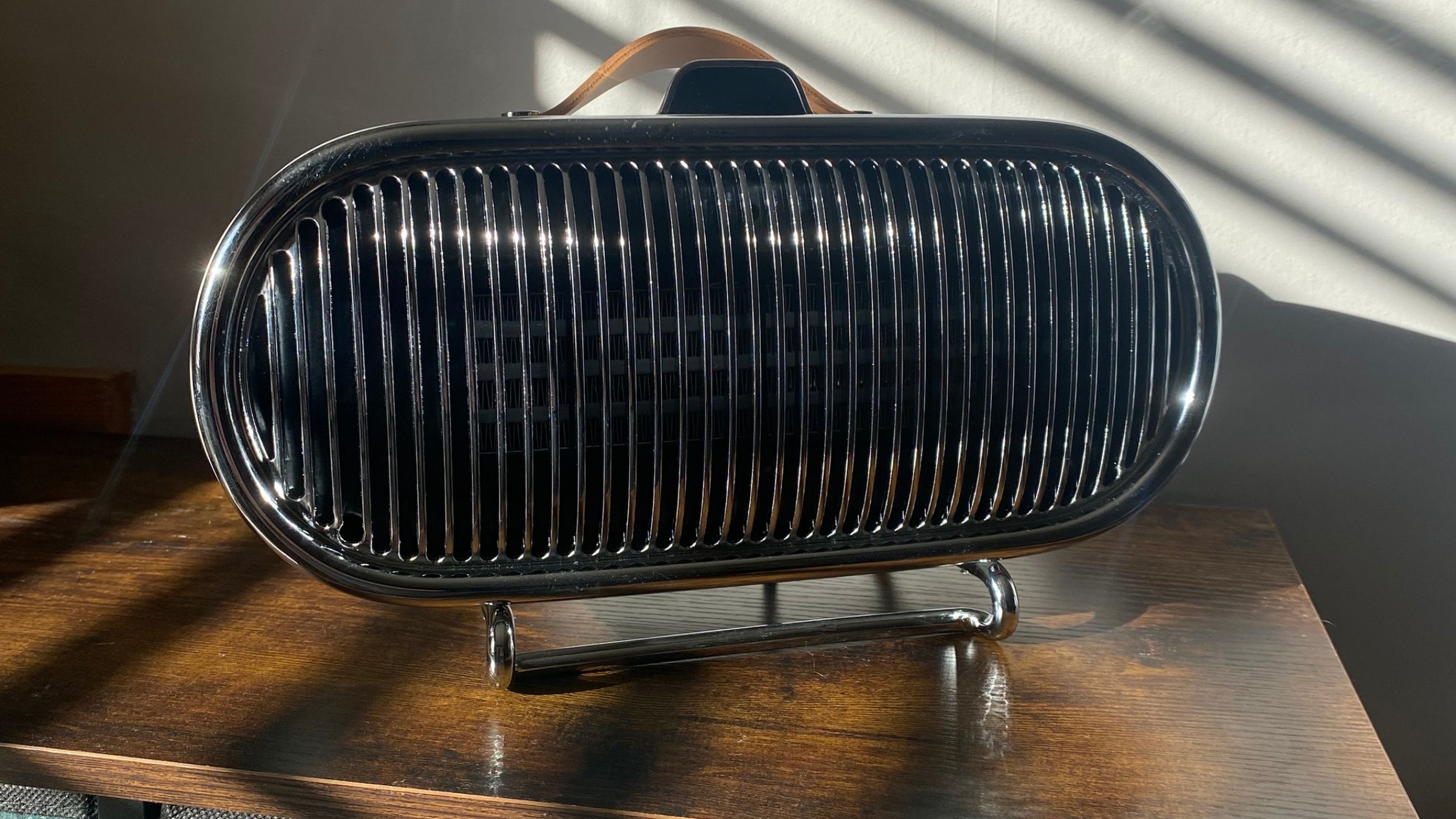 Swan 1.5kW Retro Ceramic Heater sitting on a sideboard with sunlight bouncing off the chrome grille