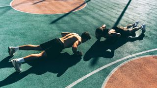Two men perform push-ups on a basketball court