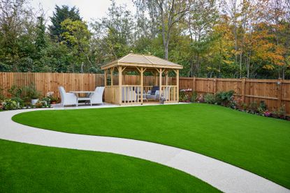 A backyard with a green lawn and a winding path leading up to a pergola 