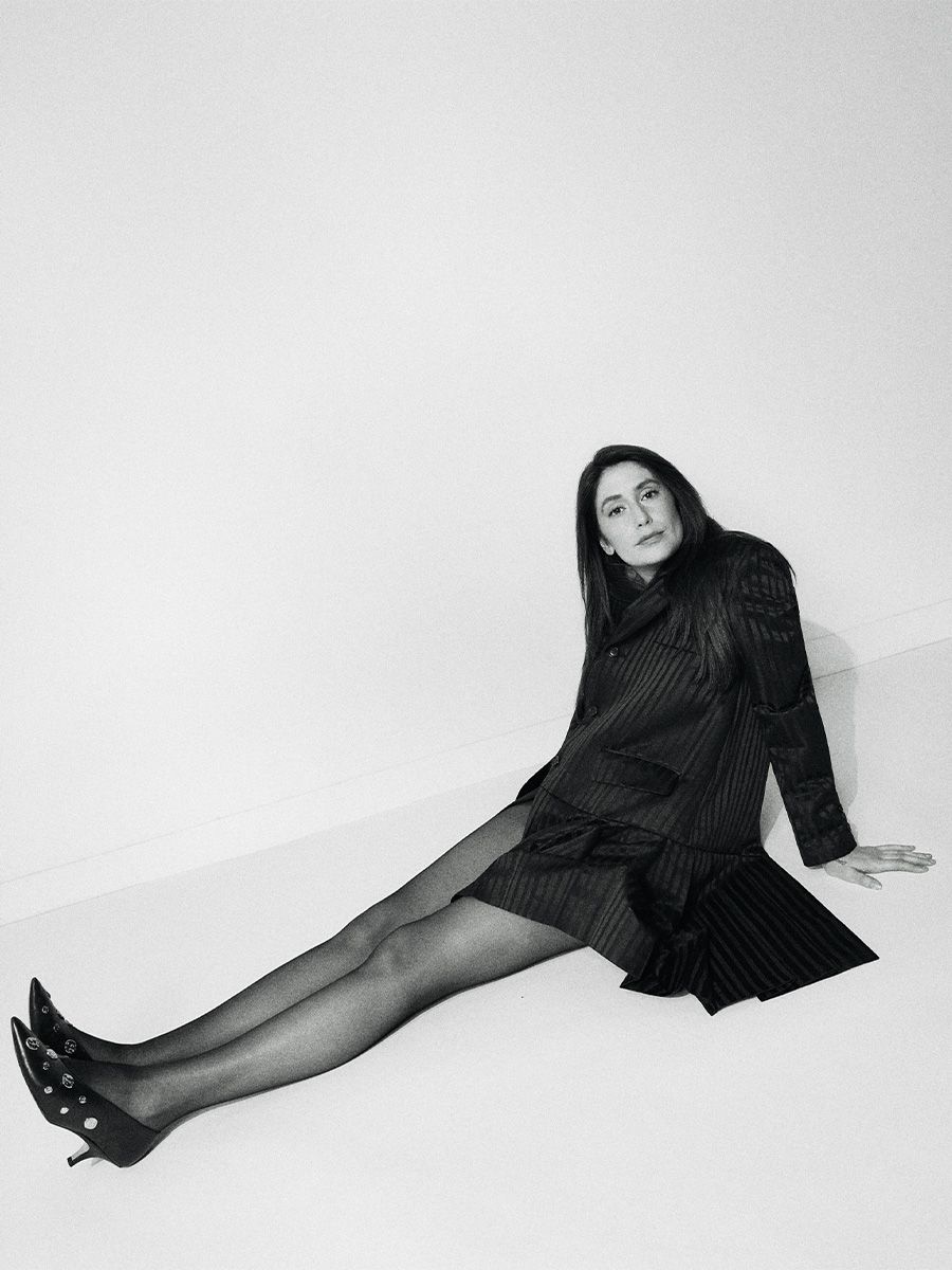 Images of Rooster actress Charly Clive shot by Emily Soto. The black and white photos show Charly sitting on the ground wearing a black pinstripe blazer dress with black heels with metal detailing.