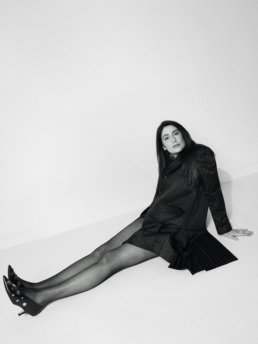 Images of Rooster actress Charly Clive shot by Emily Soto. The black and white photos show Charly sitting on the ground wearing a black pinstripe blazer dress with black heels with metal detailing.