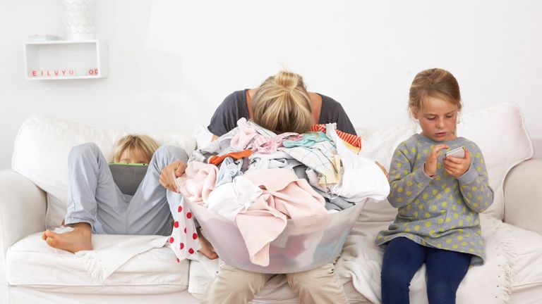 Exhausted mother with laundry basket on couch with children using digital tablet and cell phone - stock photo