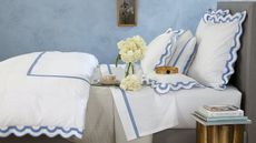 Matouk is one of the best places to buy bedding. Here is their Lowell Linen Sheet Set on a bed against a light blue wall.