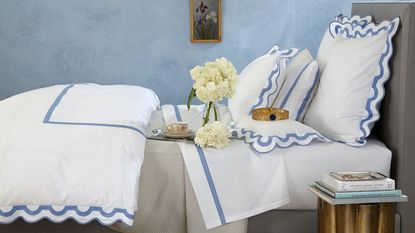 Matouk is one of the best places to buy bedding. Here is their Lowell Linen Sheet Set on a bed against a light blue wall.