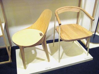Two wooden chairs (one with arm and the other armless) photographed on a white base , against a white wall
