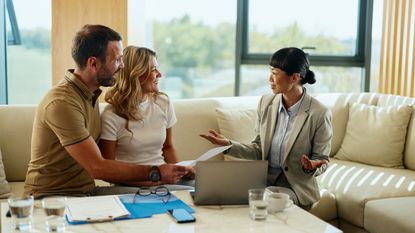 A couple consult with a financial adviser at home on their sofa.