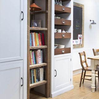 kitchen area with white wall and cabinet with books and wooden chair.