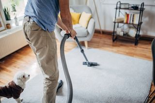 A man hoovering his rug in his home.