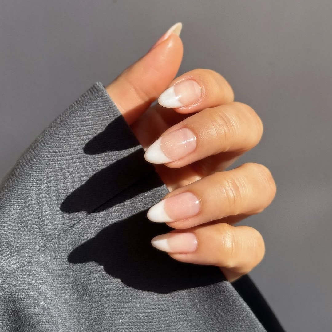 A hand in a gray suit jacket with a classic French manicure.
