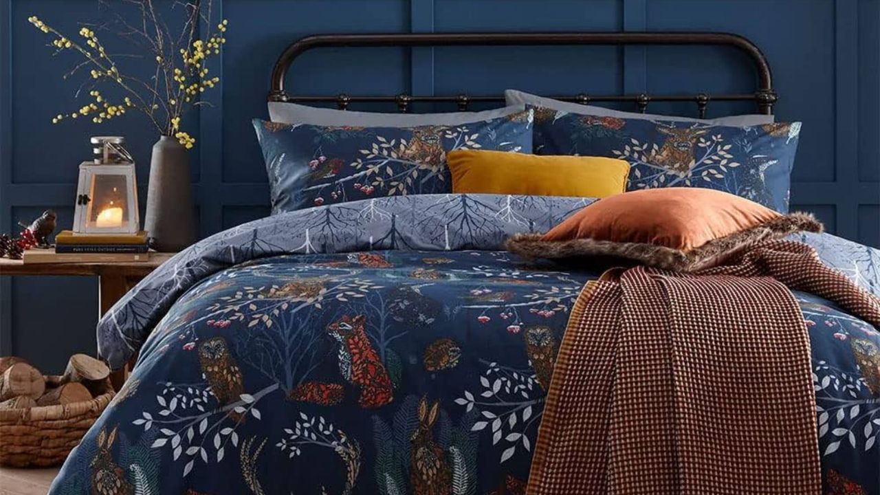 Furn Forest Fauna bed sheets on a bed with blue, orange and yellow cushions against a blue back wall.