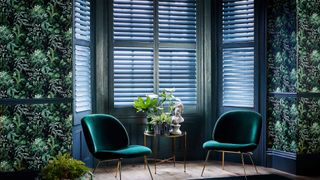 Living room with green shutters and dark leaf print wallpaper