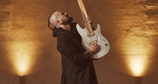 Ben Lechuga wears dark robes, leans back and plays his custom fretless Aristides electric