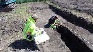 Two men working at an excavation site next to a hole in the ground.