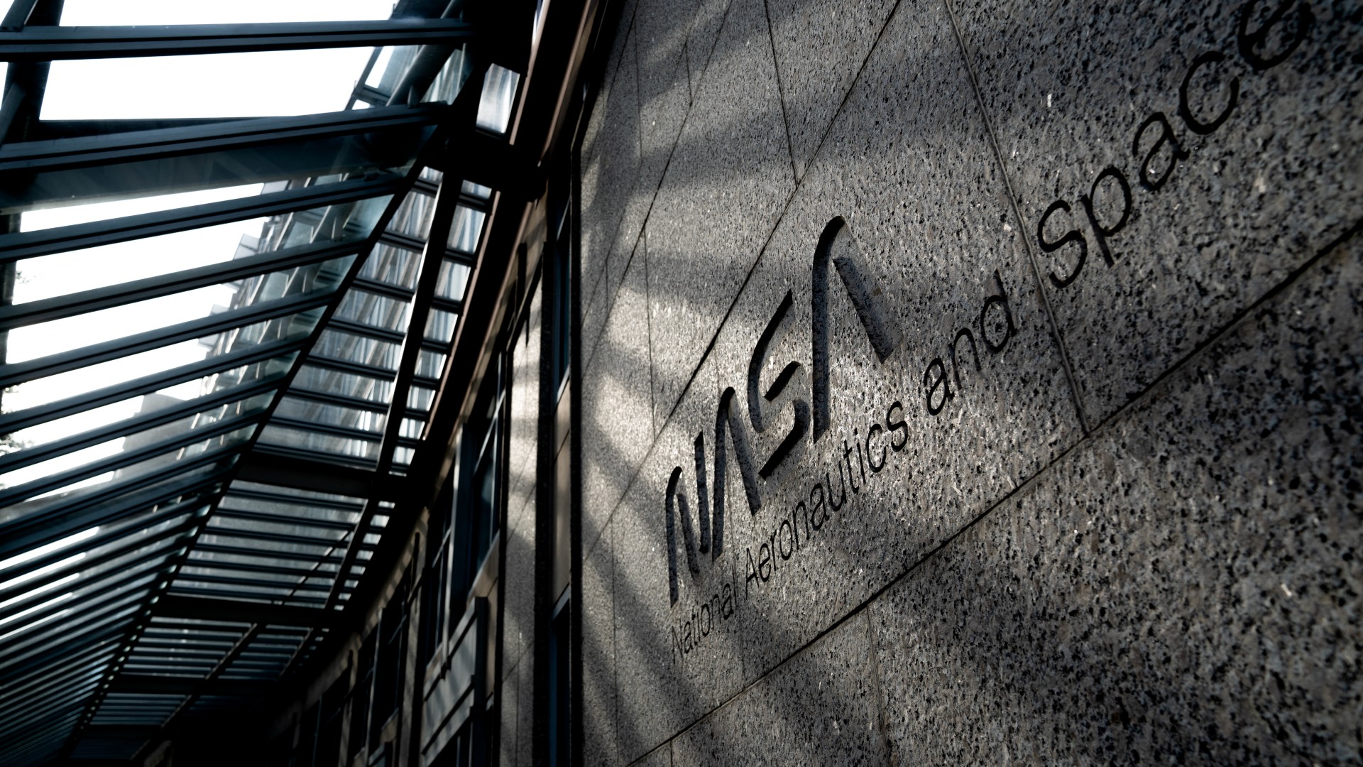the words "nasa national aeronauts and space administration" are etched into the stone facade of a building under a glass awning