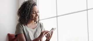 woman by window smiling as she looks at her smartphone