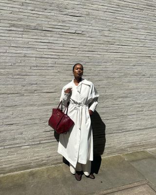 Marilyn Nwawulor-Kazemaks wearing a white trench coat and a burgundy bag.