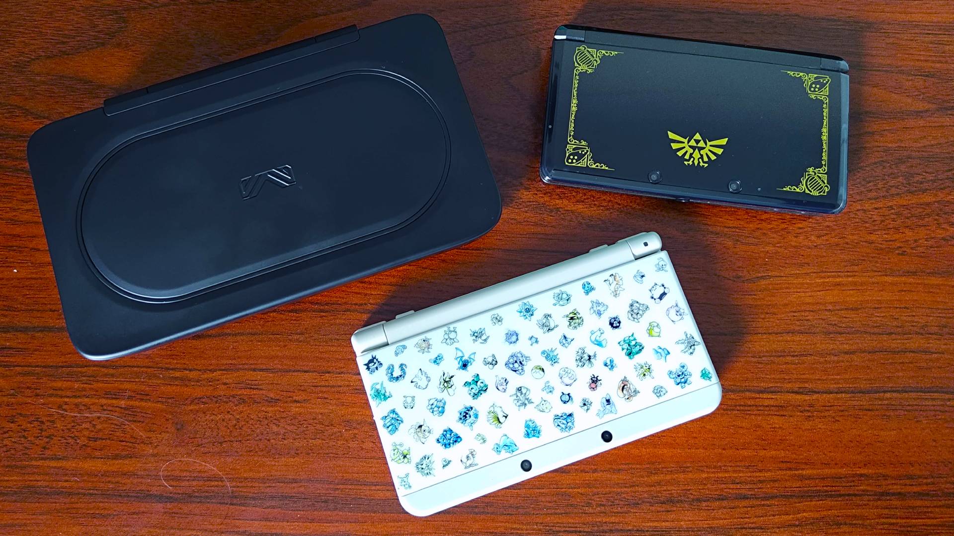 Zelda 3DS, New 3DS with Pokemon sprites cover, and Ayaneo Flip DS on woodgrain desk.