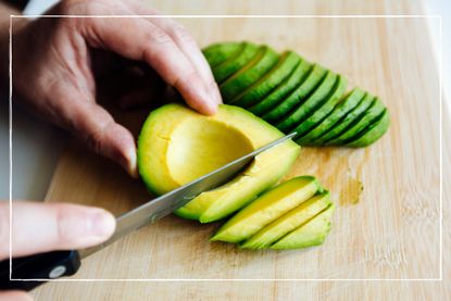 close up of hands using a knife to slice avocado