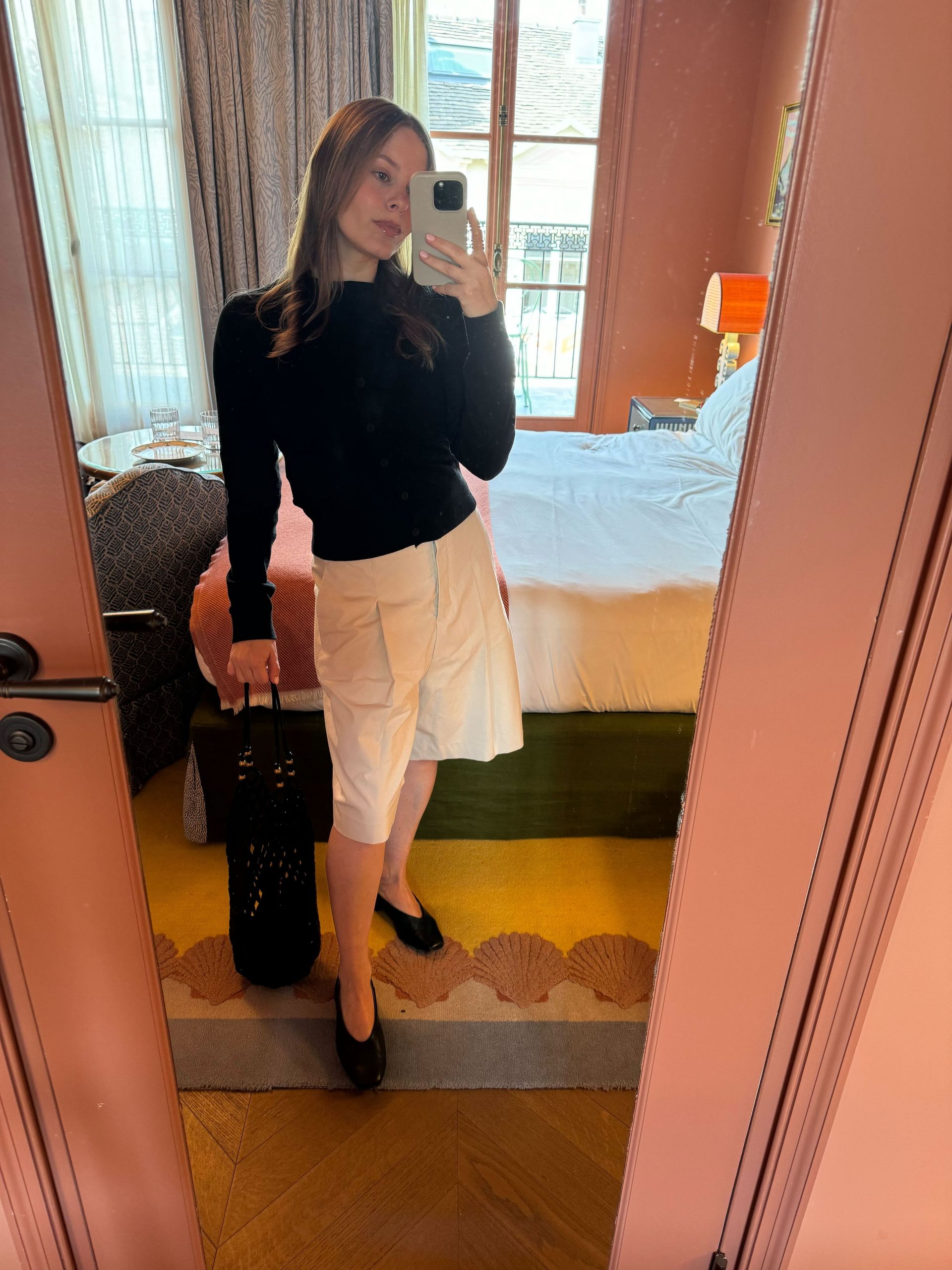 Nikki wears a black sweater, long bermuda shorts, and black ballet flats.