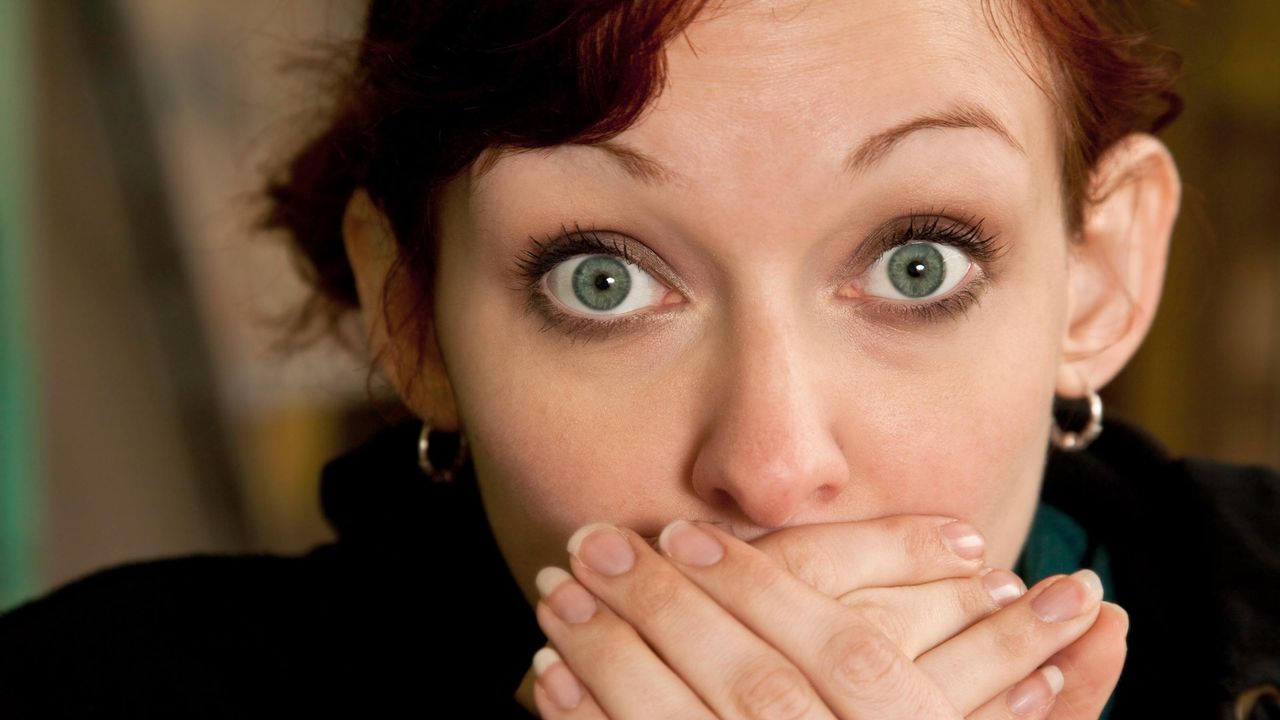 A woman with raised eyebrows covers her mouth with her hands.