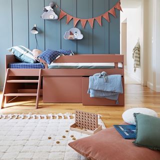 A terracotta pink storage bed in a kids bedroom with a teal blue panelled wall