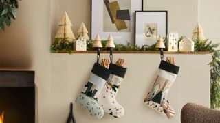 White wall in living room by a fireplace with a ledge that has Christmas decor on it. Stockings with scenes of NYC in the winter are hanging fro the ledge