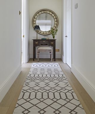 A hallway carpet idea with white walls, mirror and table, with Weaver Green's white and brown Tangier runner