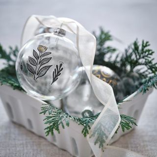 Glass Christmas bauble with flower motif and ribbon in a box with foliage