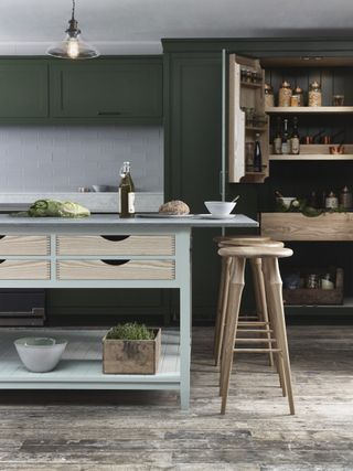 dark green kitchen with light freestanding island and wooden bar stools