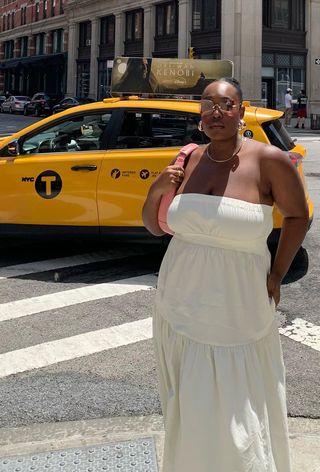 A woman's white dress outfit with strapless maxi styled with hoop earrings, a gold chain, rimless sunglasses, and a pink shoulder bag.