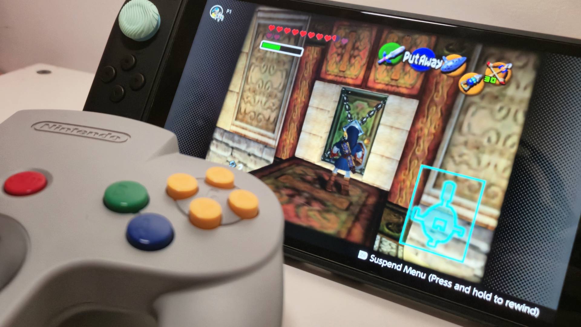 Photo of the N64 controller sitting infront of a Switch 2 running the Water Temple of Ocarina of Time.