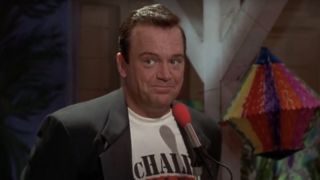 Tom Arnold smirking in front of a microphone in McHale's Navy