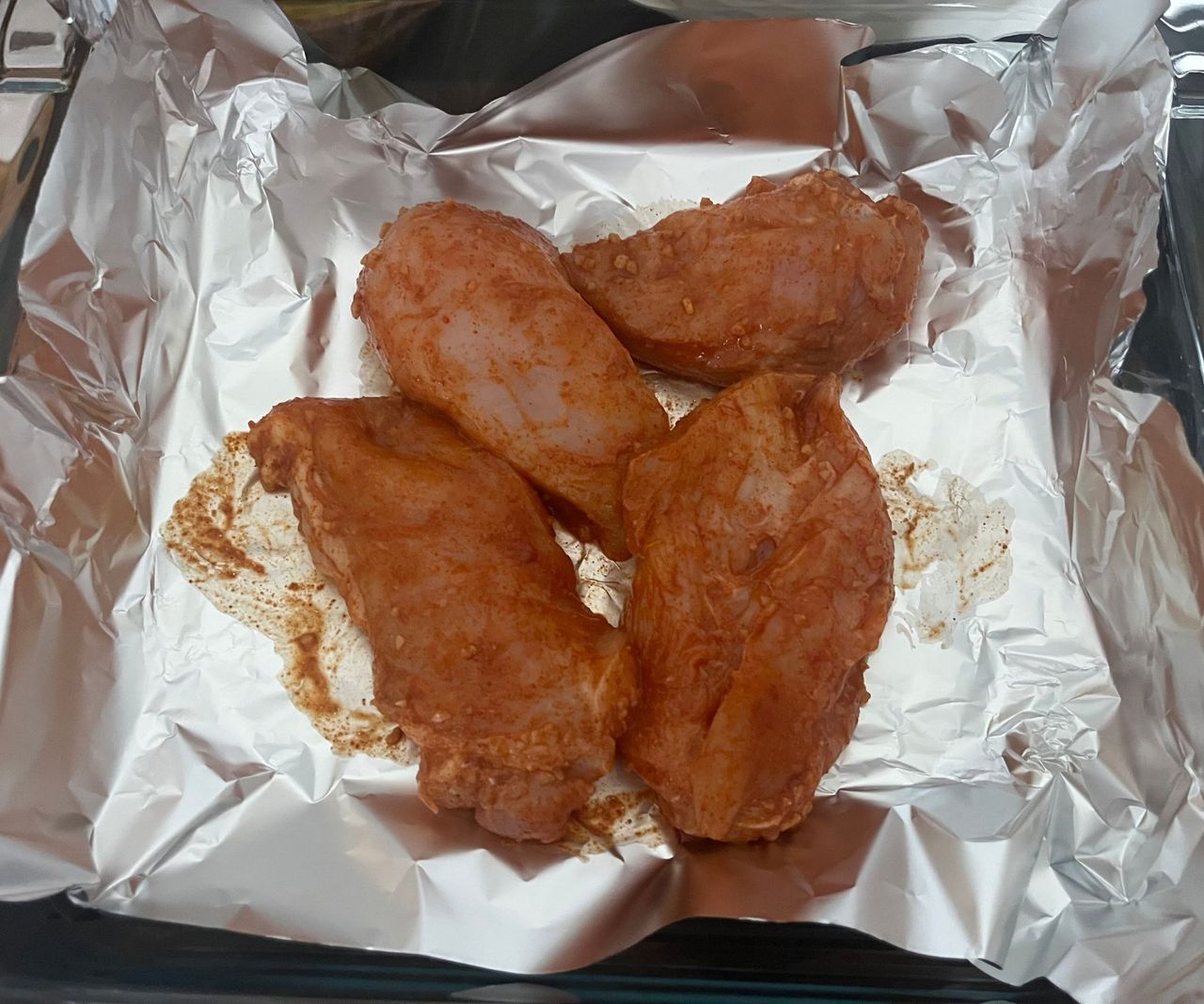 Four large marinated chicken breasts on foil