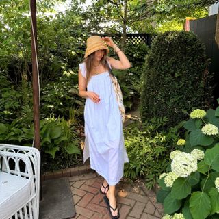 @trendingwithtinsley wearing a straw bucket hat, white cotton dress, and flip flops.