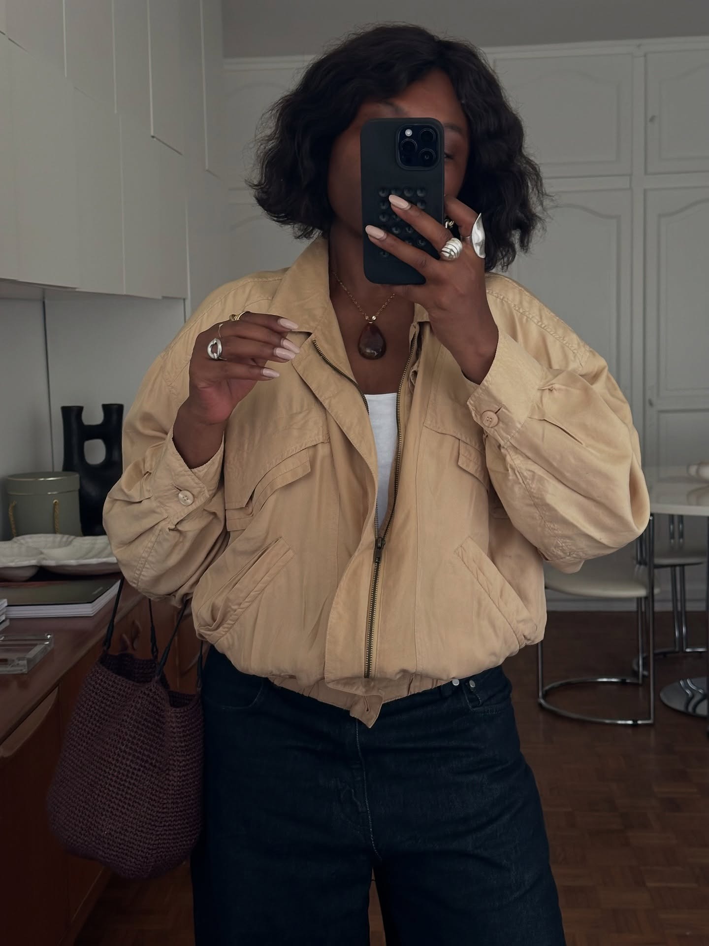 A woman with a voluminous bob haircut taking a mirror selfie wearing a &#039;90s style bomber jacket