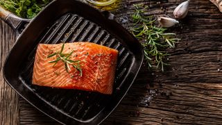 Salmon on cast iron skillet on wooden table with vegetables