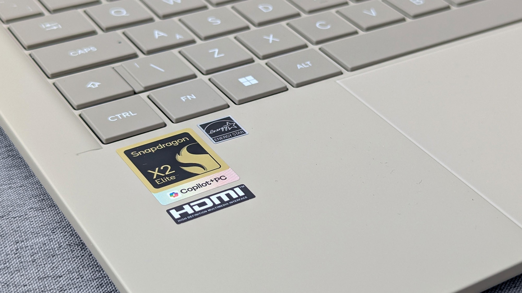 Close-up of Zenbook A14 palm rest with Snapdragon X2 Elite, Copilot+ PC, HDMI, and Energy Star stickers beside light-colored keys.