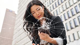 A woman picking up her dropped phone with a cracked overlay on the image