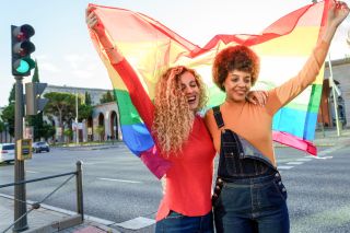 Pride events 2021: Lesbian women couple in the city with gay pride rainbow flag