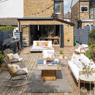 garden decking area with seating and table, in front of house with open French doors