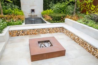 Sunken garden stone patio with corten steel firepit fire pit raised beds and water feature and garden bench with log storage