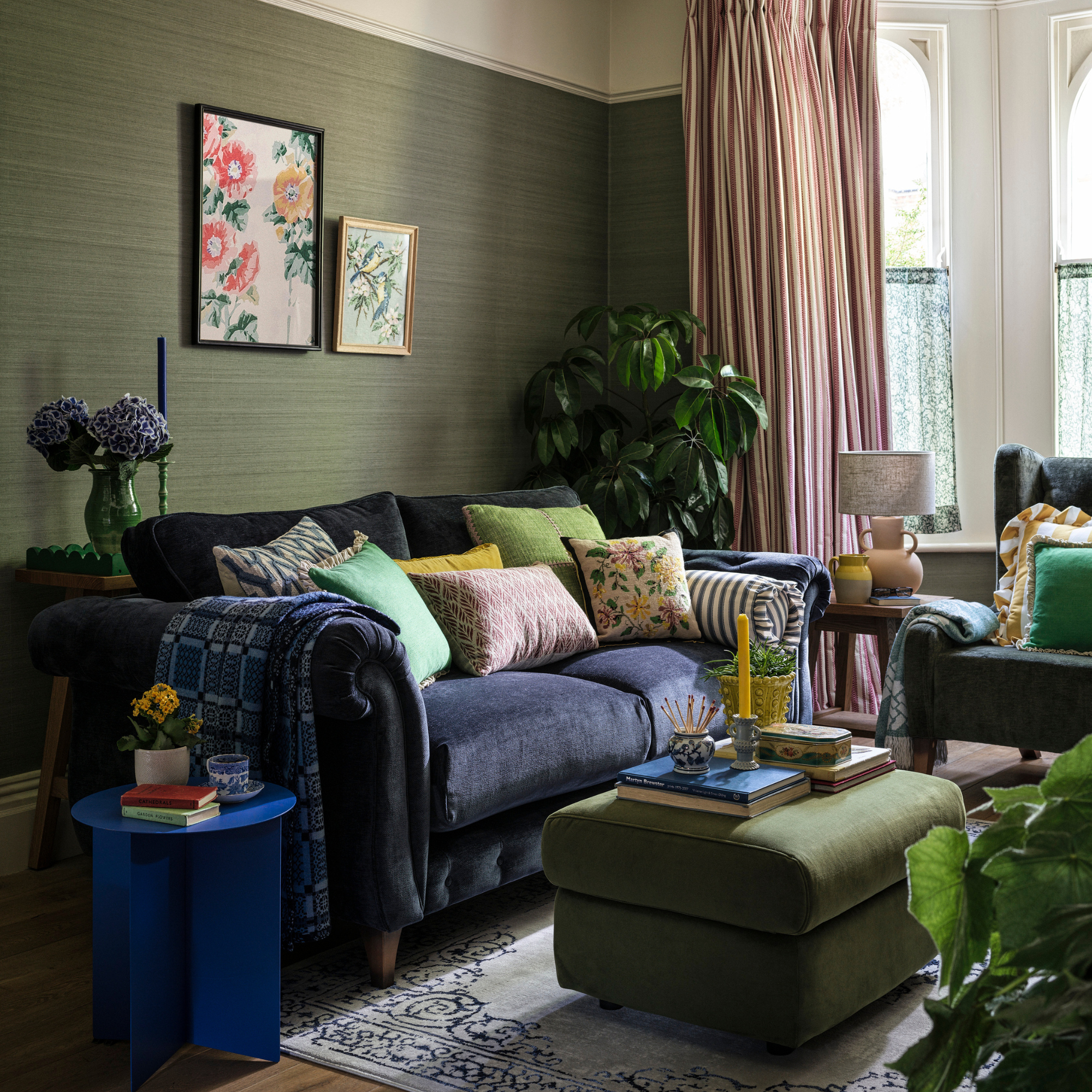a green living room with blue velvet sofa and lush, green plants